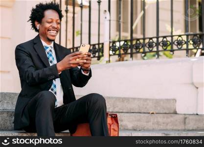 Businessman on a video call with his mobile phone while sitting on stairs outdoors. Business and technology concept.