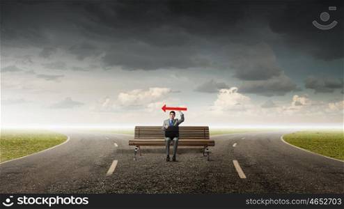 Businessman on bench. Young smiling businessman sitting on bench with briefcase and arrow in hand