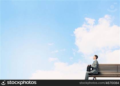 Businessman on bench. Young smiling businessman sitting on bench with briefcase in hands