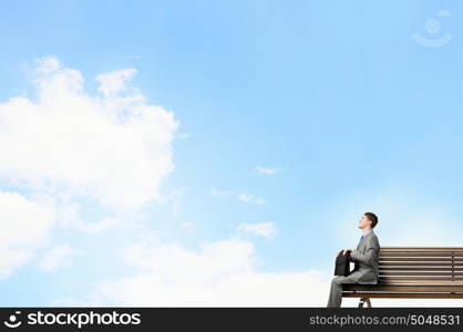 Businessman on bench. Young smiling businessman sitting on bench with briefcase in hands