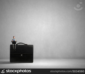 Businessman on big suitcase. Young smiling businessman sitting on giant briefcase