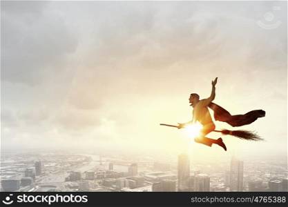 Businessman on broom. Young businessman flying high above city on broom