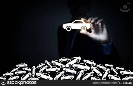 Businessman on dark background taking with fingers car icon. Man choosing car sign