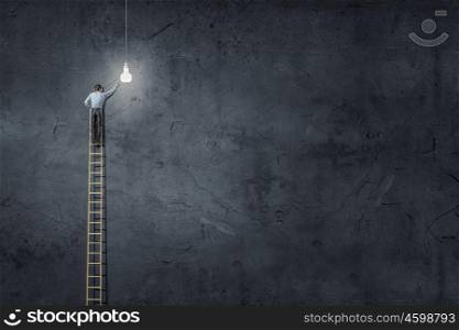 Businessman on ladder. Back view of businessman standing on ladder and reaching light bulb