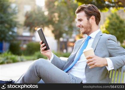Businessman On Park Bench With Coffee Using Digital Tablet