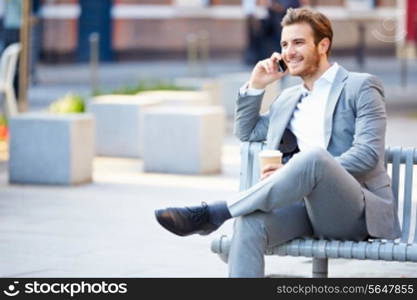 Businessman On Park Bench With Coffee Using Mobile Phone