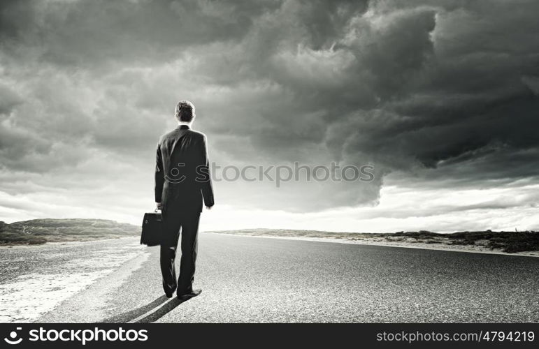 Businessman on road. Rear view of businessman with suitcase standing on road