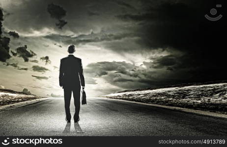 Businessman on road. Rear view of businessman with suitcase standing on road