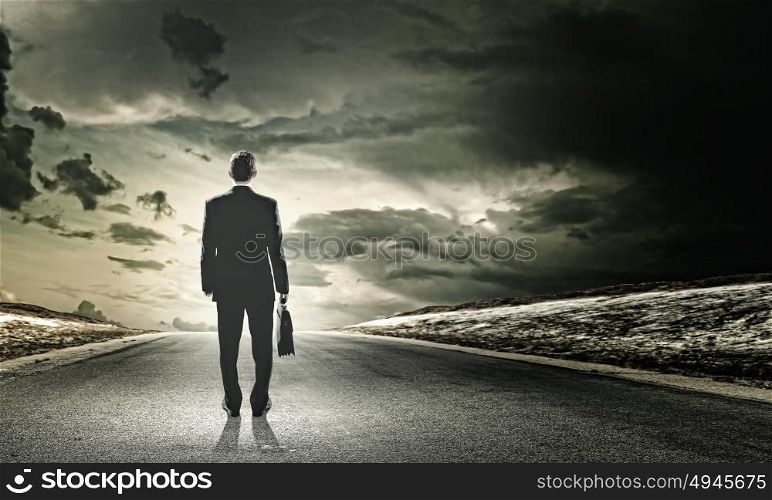 Businessman on road. Rear view of businessman with suitcase standing on road