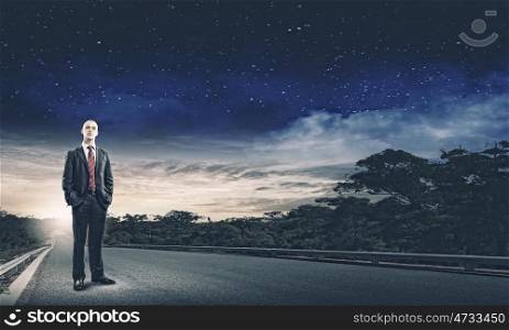 Businessman on road. Young handsome businessman standing on asphalt road
