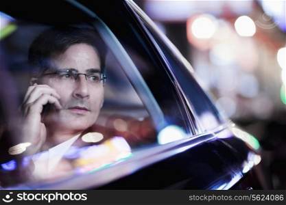 Businessman on the phone and looking out the car window at night, reflected lights