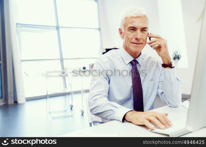 Businessman on the phone sitting at the computer in his office. Being connected and in touch