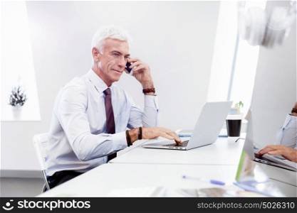 Businessman on the phone sitting at the computer in his office. Being connected and in touch