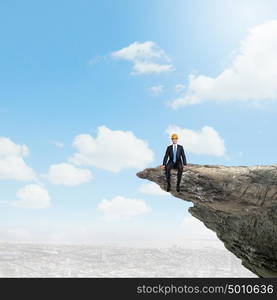 Businessman on top. Businessman in helmet sitting on edge of hill