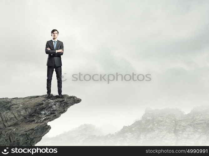 Businessman on top. Confident businessman standing on top of rock