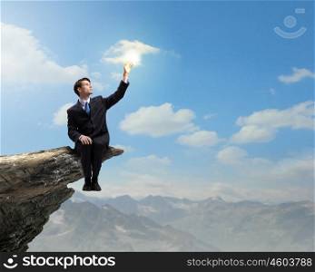 Businessman on top. Young businessman sitting on edge of rock