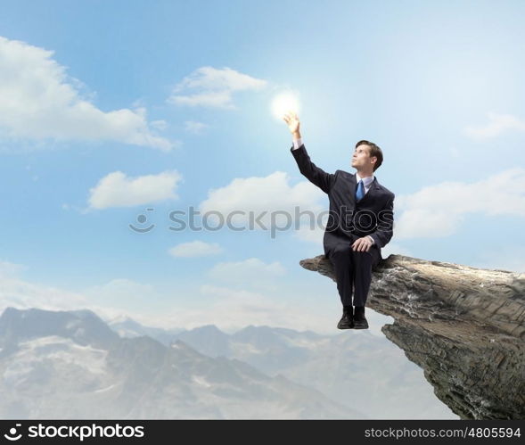 Businessman on top. Young businessman sitting on edge of rock