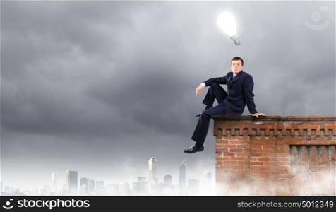 Businessman on top. Young businessman sitting on roof of building
