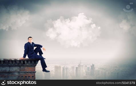 Businessman on top. Young businessman sitting on roof of building