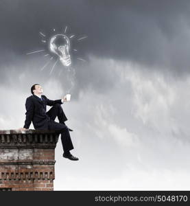 Businessman on top. Young businessman sitting on roof of building