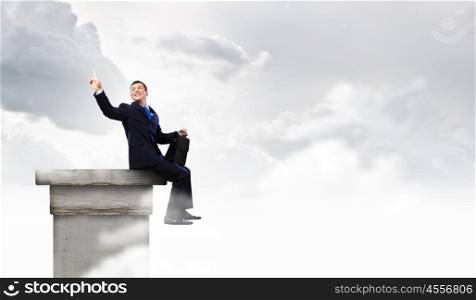 Businessman on top. Young businessman with suitcase sitting on roof of building