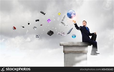 Businessman on top. Young businessman with suitcase sitting on roof of building