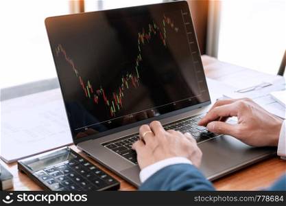 businessman or broker looking at computer laptop analysing about stock market invest trading stocks graph analysis candle line in office room.