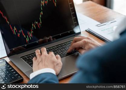 businessman or broker looking at computer laptop analysing about stock market invest trading stocks graph analysis candle line in office room.