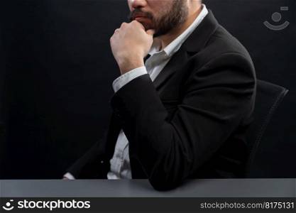 Businessman or lawyer wearing formal black suit sitting at table on isolated black background. Concept of a man with authority and seriousness gesture. equility. Businessman or lawyer wearing formal black suit sitting at table. equility