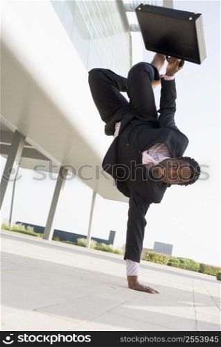 Businessman outdoors by building standing on one hand smiling