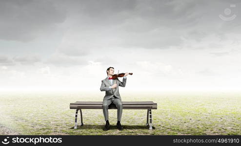 Businessman play violin. Young man in suit sitting on bench and playing violin