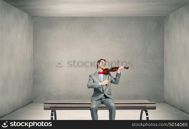 Businessman play violin. Young man in suit sitting on bench and playing violin