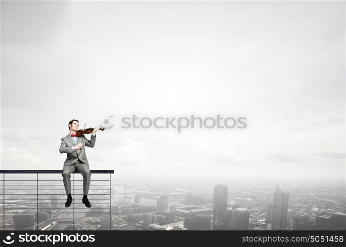 Businessman play violin. Young man in suit sitting on bench and playing violin