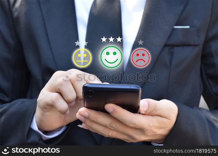 Businessman pressing face emoticon in smartphone at display on virtual screen. Concept of customer service satisfaction evaluation and feedback.