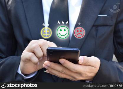 Businessman pressing face emoticon in smartphone at display on virtual screen. Concept of customer service satisfaction evaluation and feedback.
