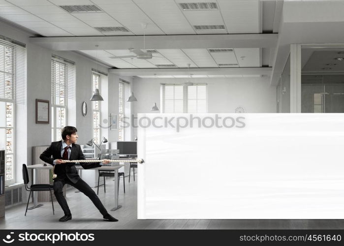 Businessman pulling banner. Young businessman in office and blank banner. Place for text