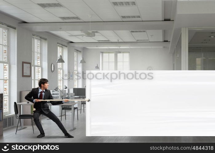 Businessman pulling banner. Young businessman in office and blank banner. Place for text