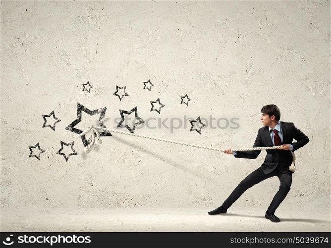 Businessman pulling rope. Image of young businessman pulling stars with rope