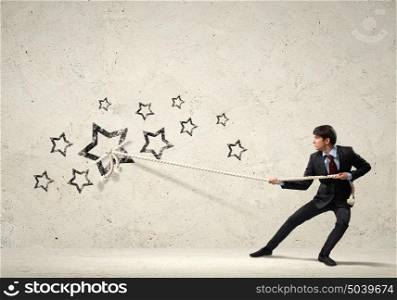 Businessman pulling rope. Image of young businessman pulling stars with rope