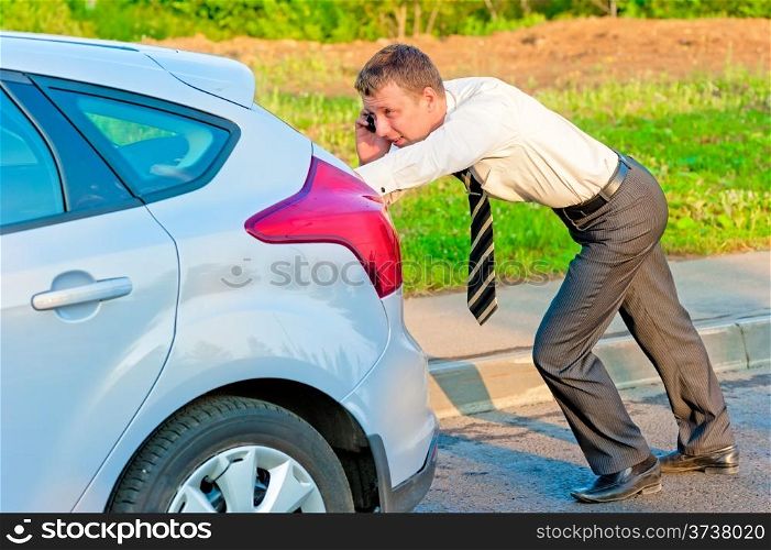 Businessman pushing a car and talking on the phone