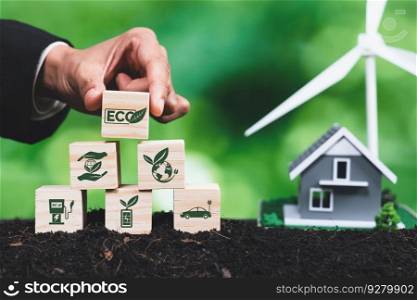 Businessman put ECO cube symbol on pyramid top stack with house and wind turbine model. Forest regeneration and natural awareness for green environment by using alternative clean energy. Alter. Businessman put ECO symbol on pyramid top with house and wind turbine. Alter