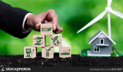 Businessman put ECO cube symbol on pyramid top stack with house and wind turbine model. Forest regeneration and natural awareness for green environment by using alternative clean energy. Alter. Businessman put ECO symbol on pyramid top with house and wind turbine. Alter