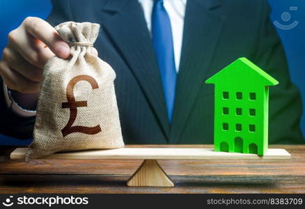 Businessman puts british pound sterling money bag on scales and green house. Investment in renovation. Reduced CO2 emissions, energy efficiency. Profitability housing of eco technologies.