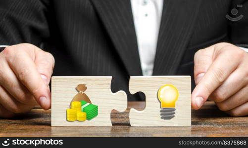 Businessman puts two puzzles with the image of money and an idea bulb. Financing promising startups and crowdfunding, looking for investments to create a business. Research and technology. Grants