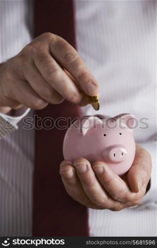 Businessman Putting Coin Into Piggy Bank