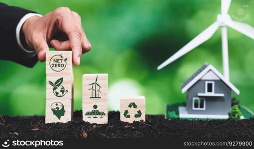Businessman putting Net Zero symbol cube on stack top for corporate environmental protection and sustainability. Modern house model power by clean wind energy with net zero CO2 emission concept. Alter. Businessman putting Net Zero symbol cube on stack top for green corporate. Alter