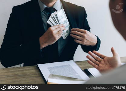 Businessman putting stack of money bills in his suit coat pocket.