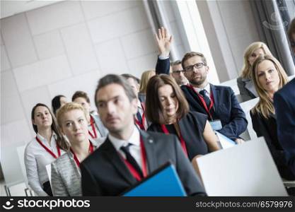 Businessman raising hand during seminar at convention center