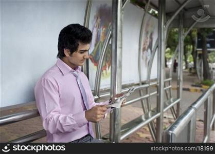 Businessman reading a newspaper at a bus stop