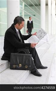 Businessman reading a newspaper outside an office building